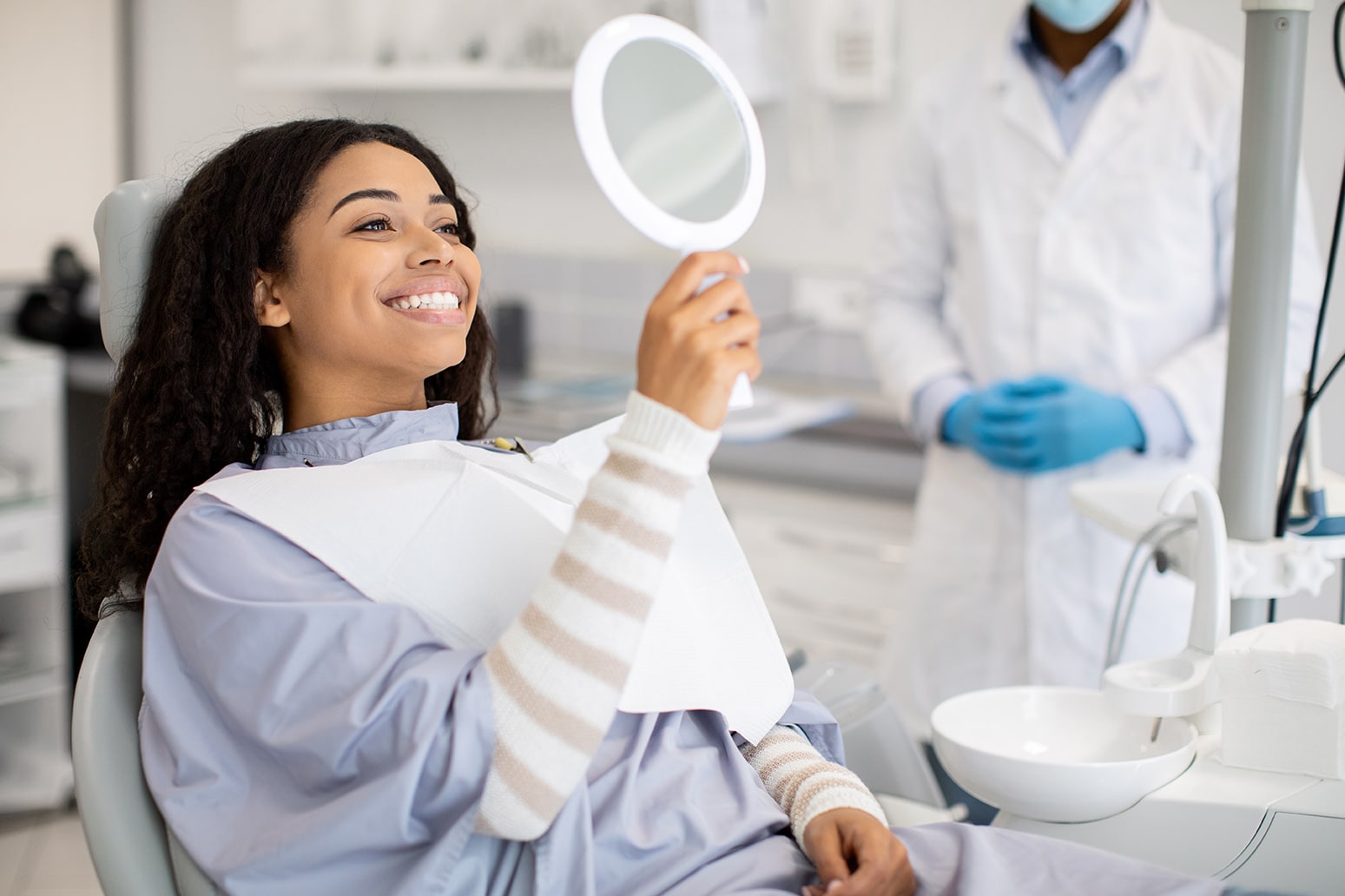 woman smiling in a mirror during cosmetic tooth bonding appointment at center ridge dental professionals